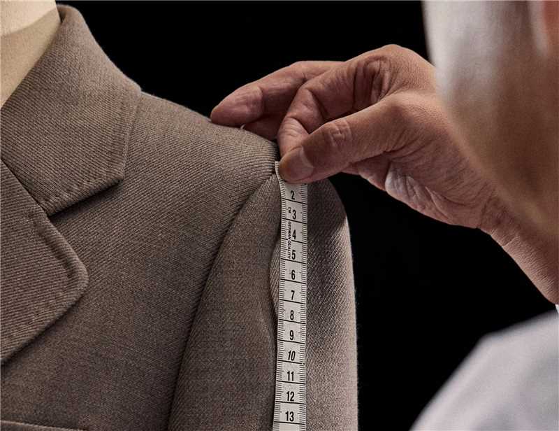 Person measuring a brown coat with a tape measure against a black background