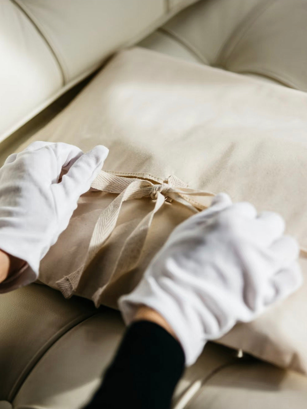 Person cleaning a beige sofa with white gloves.An image representing our services.